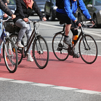 Ein roter Radwegstreifen mit drei Radfahrern, die nur ausschnittsweise zu sehen sind, die Köpfe sind oben abgeschnitten © shutterstock.com / Canetti