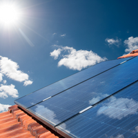 Dach mit einer Photovoltaikanlage. Über dem Dach blauer Himmel, die Sonne scheint. © Canva