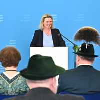 Staatsministerin Kerstin Schreyer am Mikrofon. Im Publikum sind von hinten einige Geehrte in Tracht zu erkennen © StMB